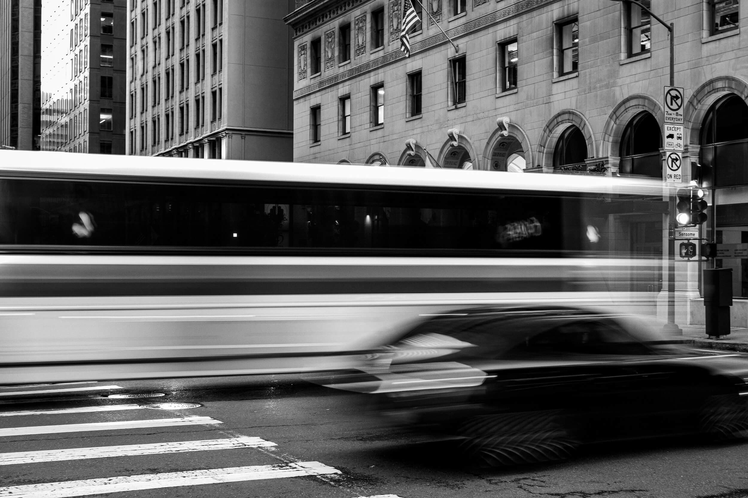 A bus and car passing through a San Francisco intersection in black and white